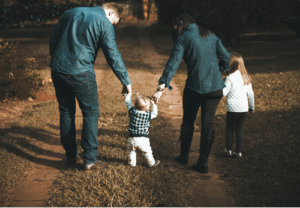 a mom and dad holding hands walking with a small child and another older child