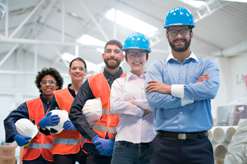 Untitled design 8 - Meixell Diehl Insurance Group of diverse engineers and construction workers wearing hard hats and orange safety vests, posing in a warehouse.